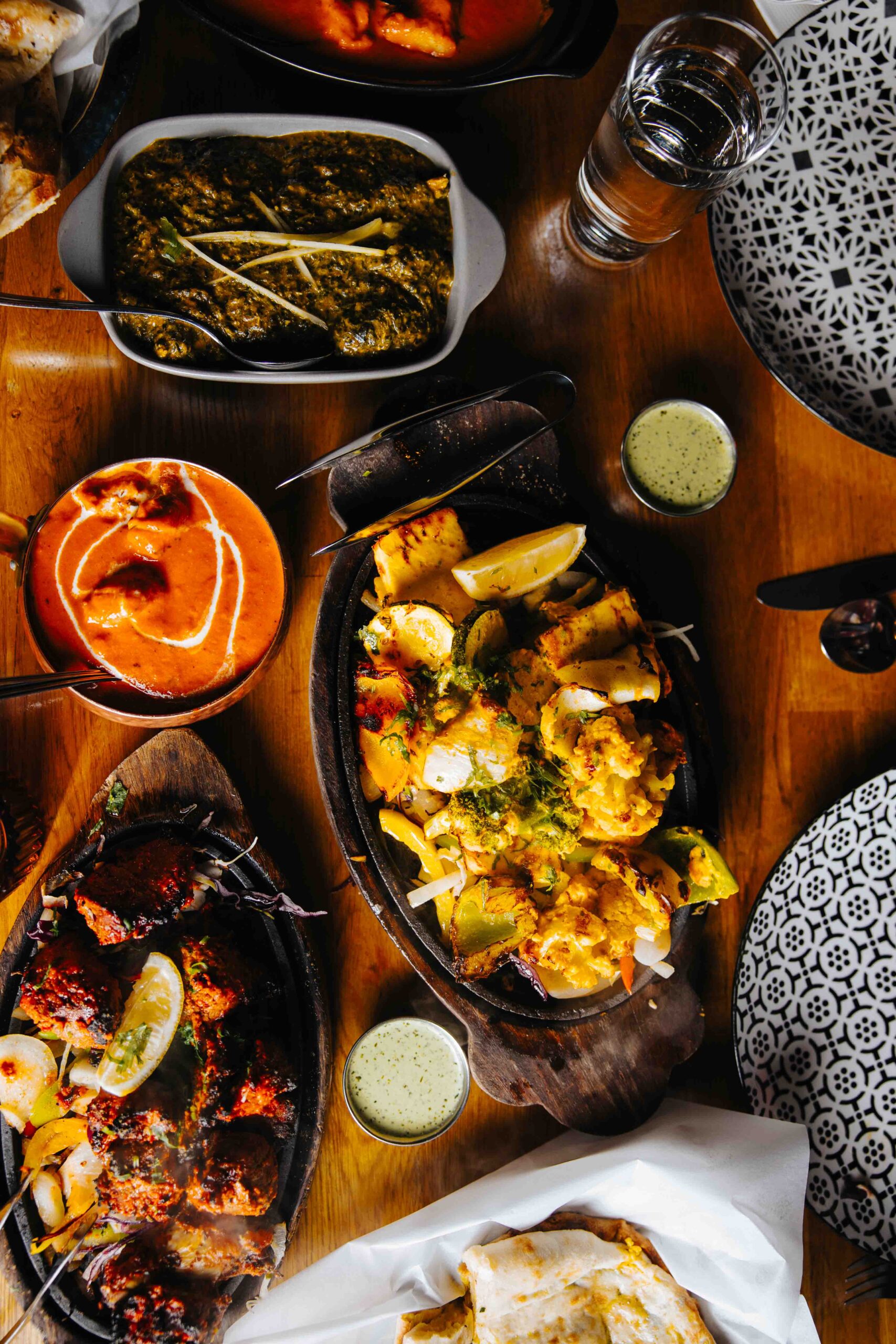 Indian cuisine spread featuring korma, madras, vindaloo, grilled dishes, naan, and assorted curries on a dining table.