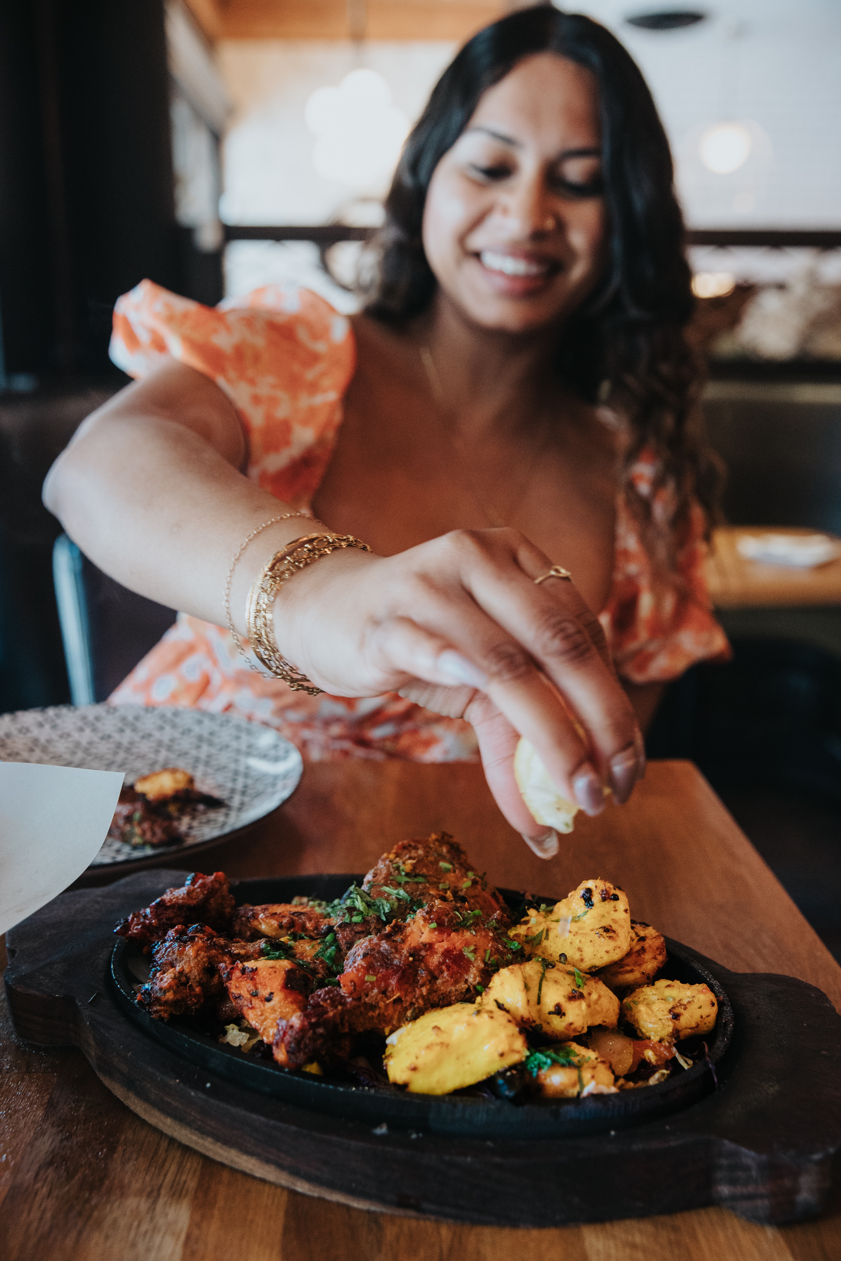 Woman enjoying a sizzling platter of grilled Indian appetizers at a restaurant.